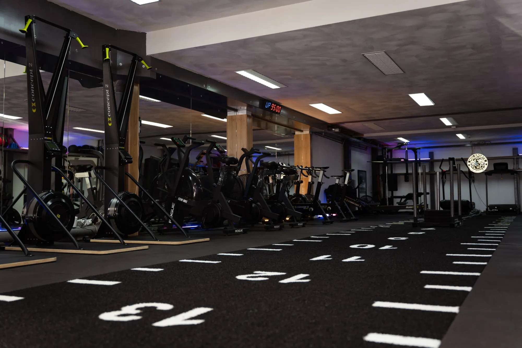 De trainingszaal van MOLSPORTS in paars licht, met de klok boven de spiegel